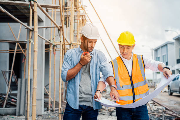 Architector and engineers with draft plan of building talking on constructing site. stock photo