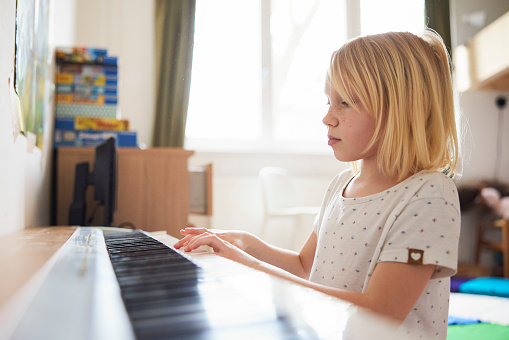 Mother teaching daughter to play piano. The girl is aged 7. Mother and girls are sitting by the old piano in a sunny room.