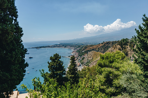 Taormina town with Mount Etna on background and many sailboats and yachts anchored in the bay close to Taormina.