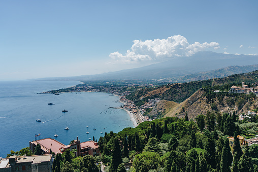 Taormina town with Mount Etna on background and many sailboats and yachts anchored in the bay close to Taormina.