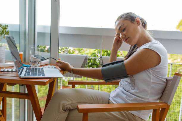 Young woman feeling weak due to the low blood pressure Copy space shot of young woman sitting at table on the balcony, eyes closed, head in hand, measuring a low blood pressure during a video conference call with her doctor. Hypotension stock pictures, royalty-free photos & images