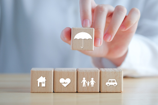 Concepto de seguro. Protección ante una posible eventualidad. Icono de paraguas sostenido a mano e icono de casa, automóvil, familia y salud en un bloque de madera para garantizar el concepto de vida. photo