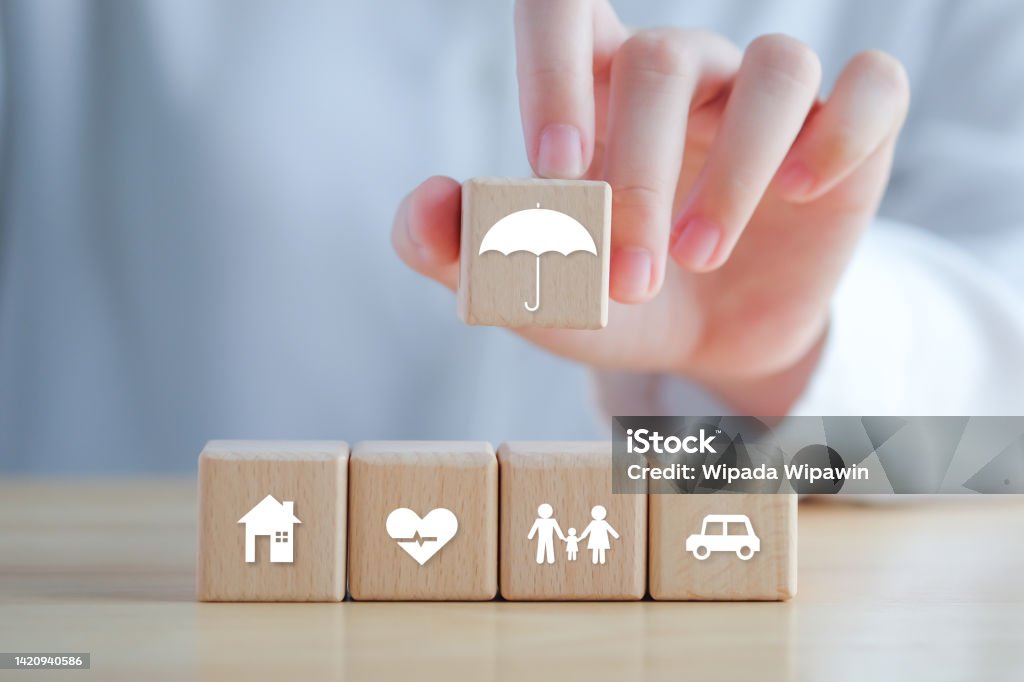 Insurance concept. Protection against a possible eventuality. Hand holding umbrella icon and House, Car, Family and Health icon on wooden block for assurance life concept. Insurance Stock Photo