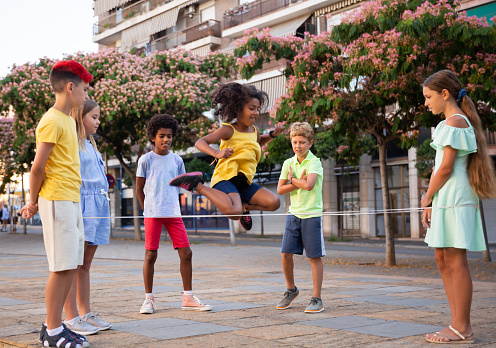 Group of kids playing with chinese jumping rope outdoors. Boys and girls having fun together.