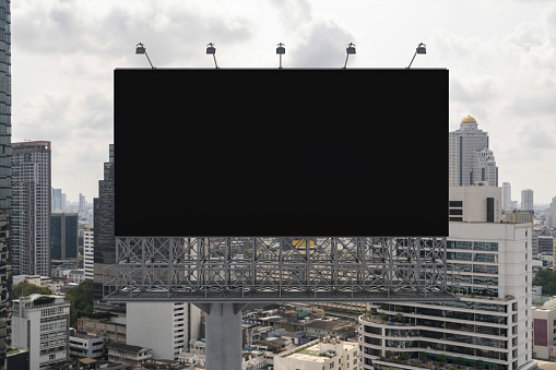 Blank black road billboard with Bangkok cityscape background at day time. Street advertising poster, mock up, 3D rendering. Front view. The concept of marketing communication to promote or sell idea.