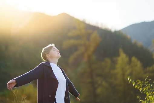 Free woman breathing clean mountain air. She open arms in happiness. Fresh air, healthy lifestyle concept.