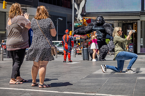 Times Square, Manhattan, New York, NY, USA - July 11th 2022: Kneeling woman taking a photograph in front of a person in a large King Kong costume