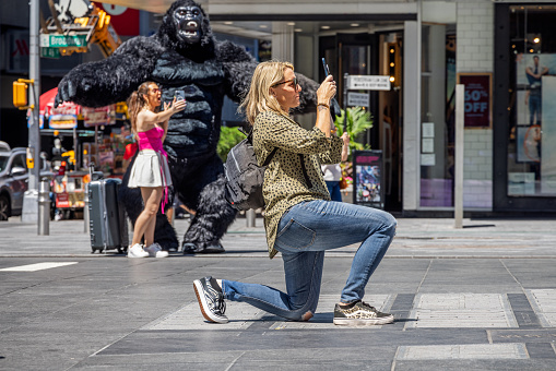 Times Square, Manhattan, New York, NY, USA - July 11th 2022: Kneeling woman taking a photograph in front of a person in a large King Kong costume