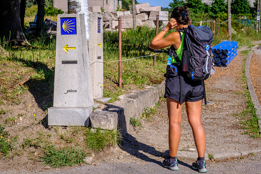 PONTEVEDRA, SPAIN - SEPTEMBER 21, 2021: A young pilgrim with a backpack observes the posts that indicate the direction to take on the Camino de Santiago.
