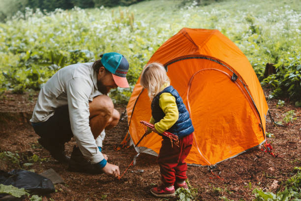 Camping family vacations child helps father to set tent travel lifestyle hiking gear tourism outdoor adventure trip stock photo