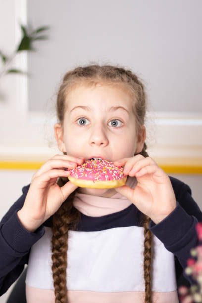 istock A girl with pigtails eats classic donuts with pink icing. 1420952252