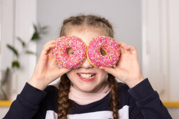 istock A girl with pigtails eats classic donuts with pink icing. 1420952280