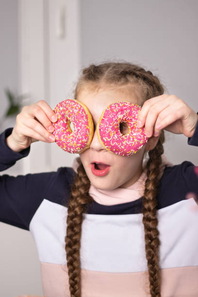 istock A girl with pigtails eats classic donuts with pink icing. 1420952282