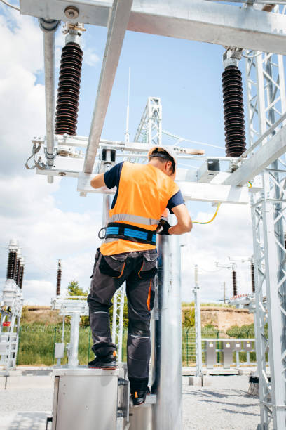 istock Electrician in protective helmet working on high voltage power lines. Highly skilled workmen servicing the electricity grid. Modern power station with power towers 1420952812