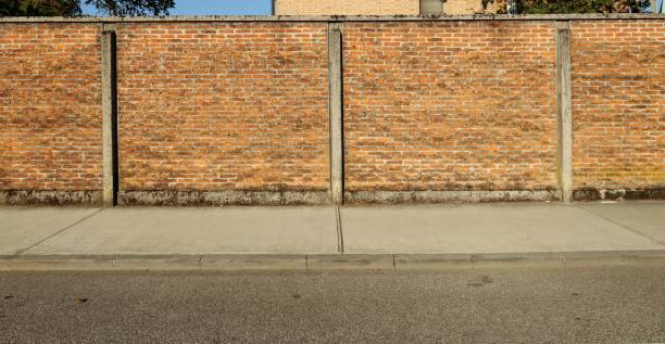 istock Brick wall with thin concrete columns. Cement sidewalk and asphalt road in front. 1420954472