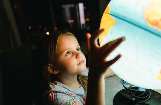 Little girl looking at globe lamp in the dark room at night