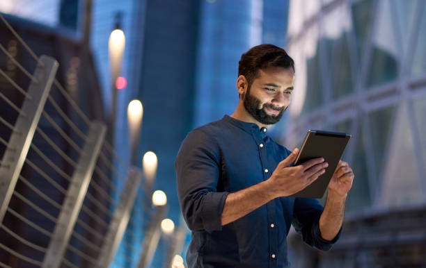 Rich successful indian business man standing using digital tablet in night city.