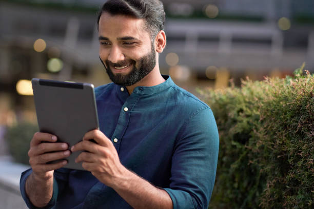 istock Smiling indian business man using digital tablet standing in night city park. 1420959432