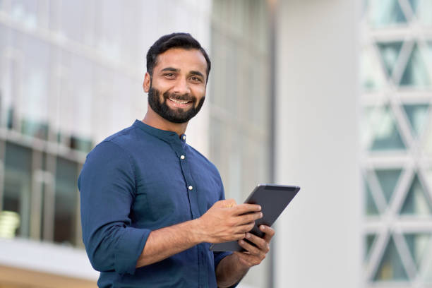 istock Smiling indian business man executive using digital tablet outdoors. 1420959436