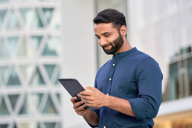 istock Smiling indian professional business man using digital tablet outdoors. 1420959489
