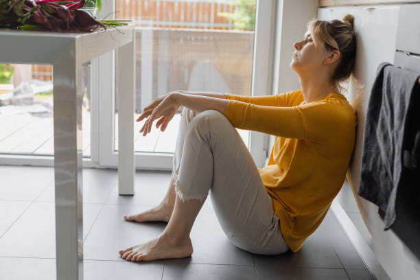 zdenerwowana kobieta siedząca w kuchni na podłodze, jest zmęczona, przepracowana, problemy rodzinne to jej demotywacja w życiu - stereotypical housewife zdjęcia i obrazy z banku zdjęć