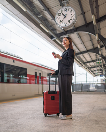 Portrait photo of a young beautiful asian businesswoman lady smile and holding on her phone on the commuter train platform waiting for the train