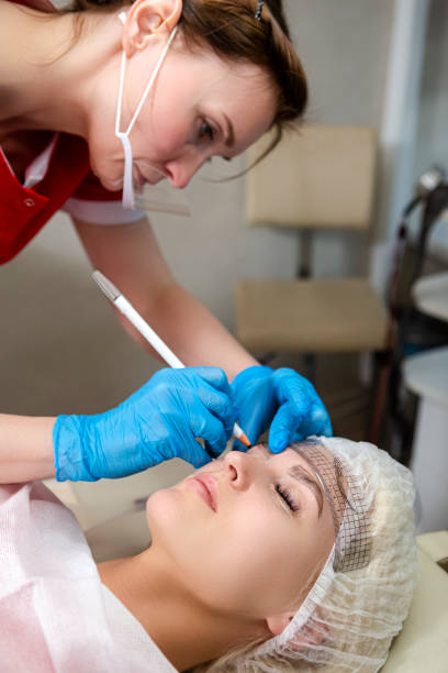 istock Closeup of Professional Female Beautician Tattooing Woman's Eyebrows Using Special Marking Equipment While Permanent Make-up Process. 1420972742