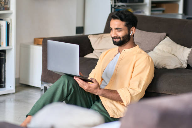 istock Happy indian man sitting at home wearing earbud using laptop computer. 1420975000