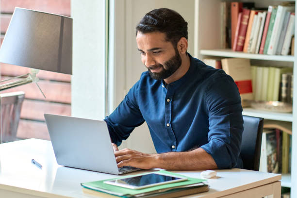 hombre de negocios indio que trabaja a distancia en una computadora portátil sentado en la oficina en casa. - master of business administration fotografías e imágenes de stock