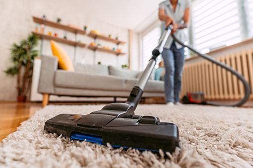 Beautiful senior woman vacuuming the carpet in her apartment. Close-up