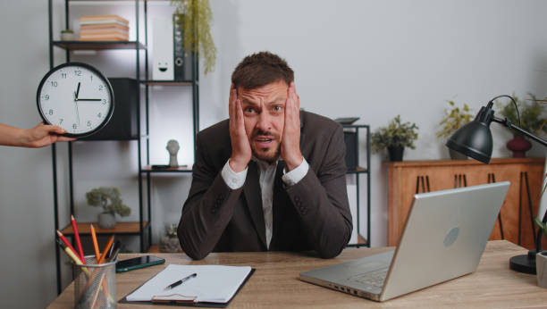 homem de negócios trabalhando em laptop no escritório com tempo de verificação de ansiedade no relógio estar atrasado, prazo - waiting wasting time time business - fotografias e filmes do acervo