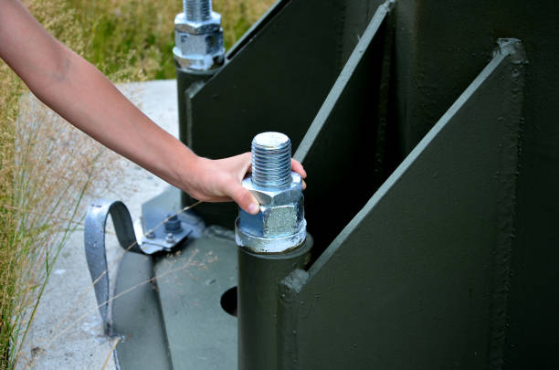 columna de acero gris, viga, atornillada con tornillos grandes masivos a la base de concreto. poste de remonte, alto voltaje, valla publicitaria en el estacionamiento. pilón cilíndrico de acero, tubo, verde, oliva, - ski lift new design tube fotografías e imágenes de stock