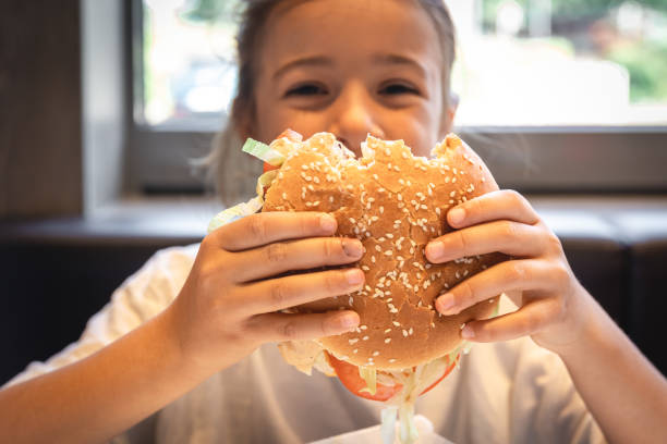 istock A little girl eats an appetizing burger, close-up. 1420977436