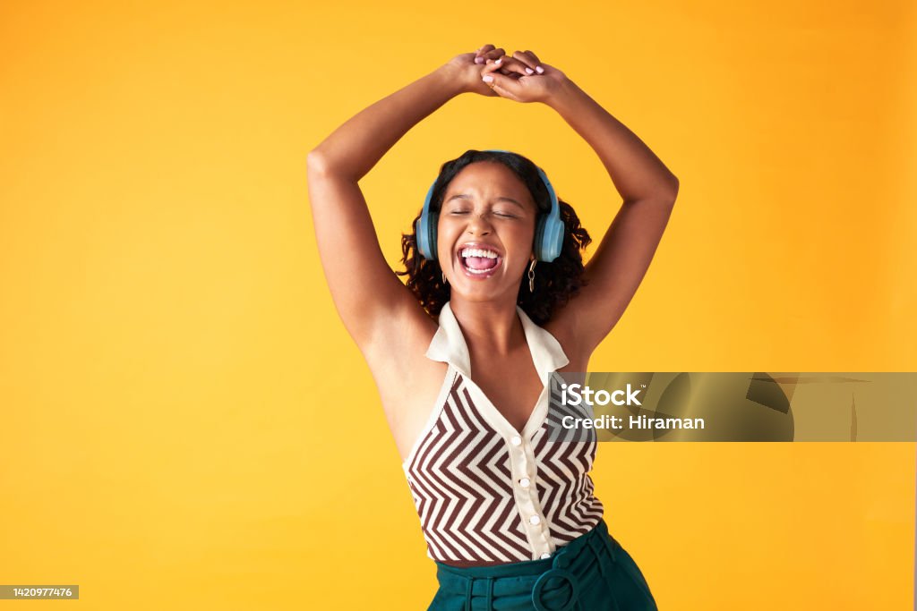 Dance, music and creative woman listening with wireless headphones in photographer studio background. Happiness, freedom and relax female singing while streaming radio or spotify in yellow backdrop Music Streaming Service Stock Photo