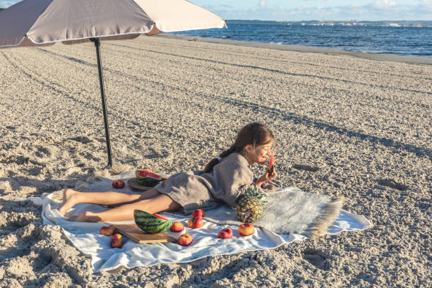 istock Little girl eats fruit lying on a blanket on the beach. 1420981983
