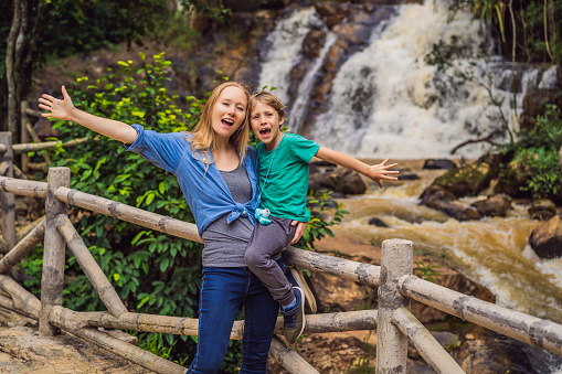 Mom and son on the background of Majestic landscape of waterfall in summer at Dalat, Vietnam.