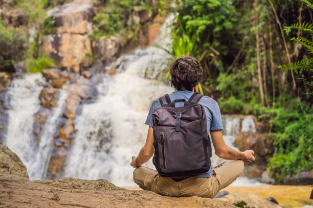 young man with backpack standing near a waterfall in forest. male hiker in the nature - bali male beautiful ethnicity imagens e fotografias de stock