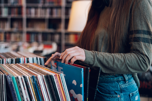 Close shot of a woman hands browsing records in the vinyl record store. Audiophile and music lover. Vintage Vinyl LP In Records Shop.