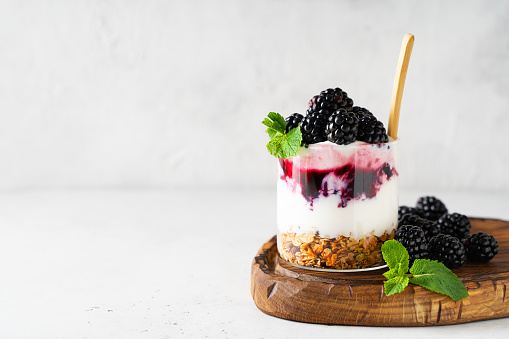 Blackberry granola yogurt dessert with berris and mint leaf on wooden cut borad on white background, copy space,