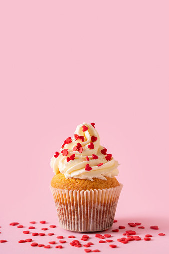 Vanilla cupcakes close up on with heart shape confectionery sprinkles on pink background, copy space, valentine day, mothers day concept, vertical