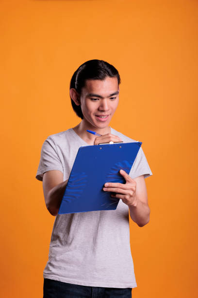istock Smiling asian man taking notes in blue clipboard 1420985071