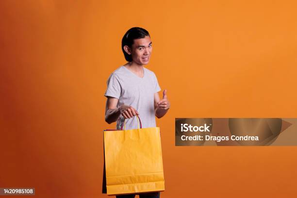 Cheerful Smiling Man Pointing At Paper Shopping Bag Stock Photo - Download Image Now