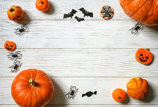 Halloween background, top view. Pumpkins and sweets on white wooden table, flat lay. Frame of Halloween orange food and decorations on wood planks with space. Design, fall, October, treat and trick.