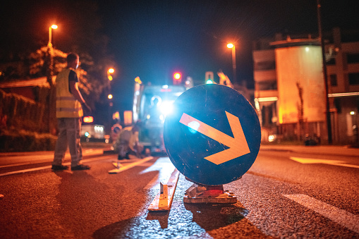 Compulsory right road sign and traffic cones before freshly painted crosswalk on the road in the middle of the city in the night.