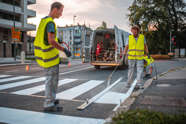 Road Construction Workers Spray Painting A Crosswalk Road construction workers spray painting a crosswalk using a stencil and a spray painter gun. All wearing a reflective vest. freshly painted road markings stock pictures, royalty-free photos & images