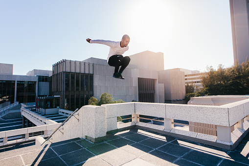 Athletic young man doing parkour tricking and freerunning over urban city background. Young sportsman practicing extreme sport activities outdoors in city.