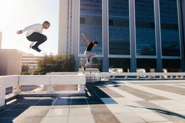 Two young sportsmen practicing parkour against a city background. Young people practicing extreme sport activities outdoors in city. Male athletes running and jumping over obstacles.