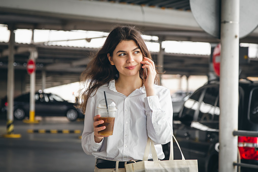 Attractive business young woman in a white shirt in a car park talking on the phone.