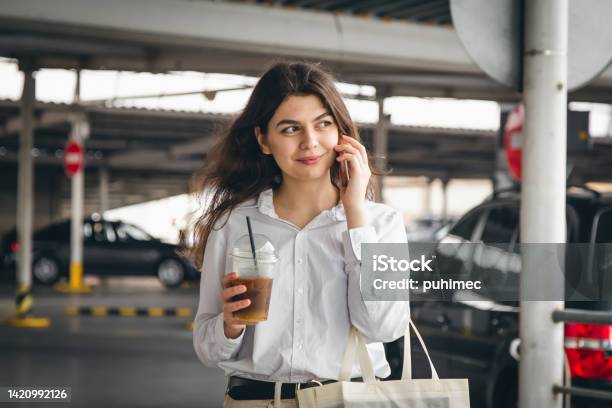 Business Young Woman With Coffee Talking Cheerfully On The Phone In The Parking Lot Stock Photo - Download Image Now