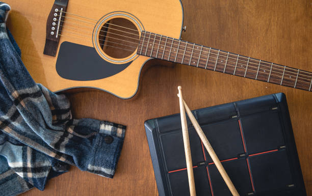 Music composition with acoustic guitar and drumsticks on wooden background, top view.
